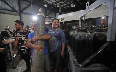 Supporters of Hezbollah carry an oxygen tank at the site of Beirut's southern suburb of Janah which Israel's Prime Minister Benjamin Netanyahu said was a weapons depot belonging to the movement on September 29, 2020. (Photo by ANWAR AMRO / AFP)