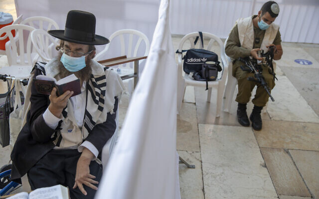 With a social distancing barrier, an ultra-Orthodox Jewish man and an Israeli soldier pray ahead of Yom Kippur at the Western Wall in Jerusalem's Old City, September 27, 2020. (AP Photo/Ariel Schalit) With a social distancing barrier, an ultra-Orthodox Jewish man and an Israeli soldier pray ahead of Yom Kippur at the Western Wall in Jerusalem's Old City, September 27, 2020. (AP Photo/Ariel Schalit)