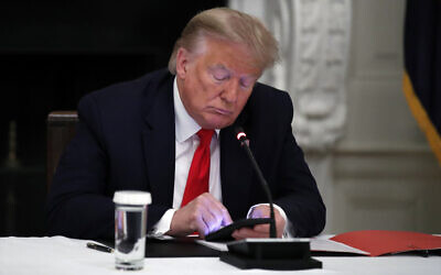 FILE -- US President Donald Trump looks at his phone during a roundtable with governors on the reopening of America's small businesses, in the State Dining Room of the White House, June 18, 2020, in Washington. (AP Photo/Alex Brandon)