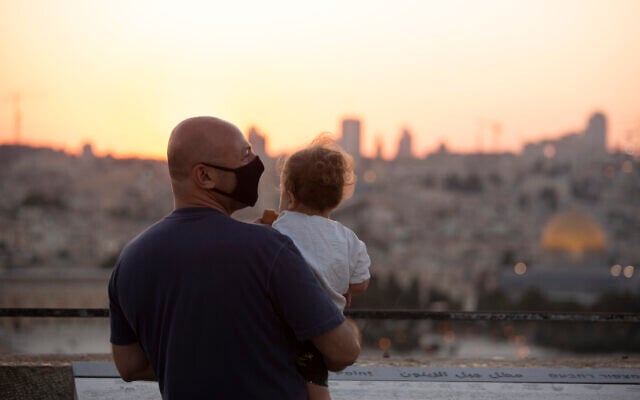 A man wearing a mask to curb the spread of the coronavirus holds a child on an overlook at the Mount of Olives as they watch the sun set behind the Dome of the Rock in Jerusalem, September 2, 2020. (AP Photo/Maya Alleruzzo)