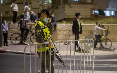 In this September 8, 2020, photo, an Israeli border policeman sets up a barrier as ultra-Orthodox Jews wearing face masks during the coronavirus pandemic wait to cross the street during an overnight curfew in Beit Shemesh (AP Photo/Ariel Schalit)