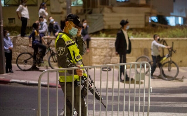 In this September 8, 2020, photo, an Israeli border policeman sets up a barrier as ultra-Orthodox Jews wearing face masks during the coronavirus pandemic wait to cross the street during an overnight curfew in Beit Shemesh (AP Photo/Ariel Schalit) In this September 8, 2020, photo, an Israeli border policeman sets up a barrier as ultra-Orthodox Jews wearing face masks during the coronavirus pandemic wait to cross the street during an overnight curfew in Beit Shemesh (AP Photo/Ariel Schalit)