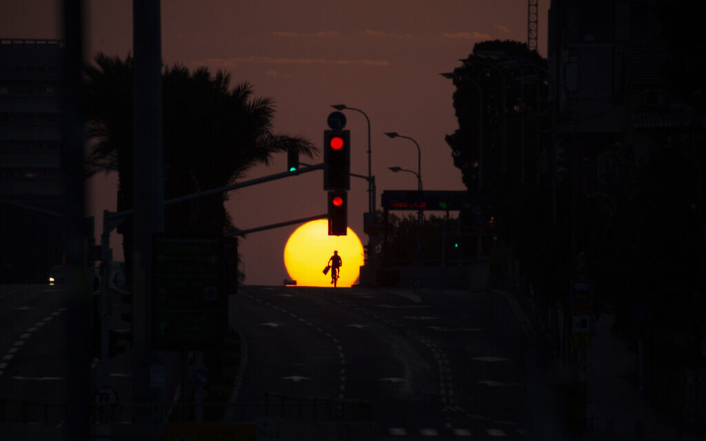A person rides a bicycle on an empty street as the sun sets on the first day of a three-week lockdown in Tel Aviv, September 18, 2020. (AP Photo/Ariel Schalit) A person rides a bicycle on an empty street as the sun sets on the first day of a three-week lockdown in Tel Aviv, September 18, 2020. (AP Photo/Ariel Schalit)