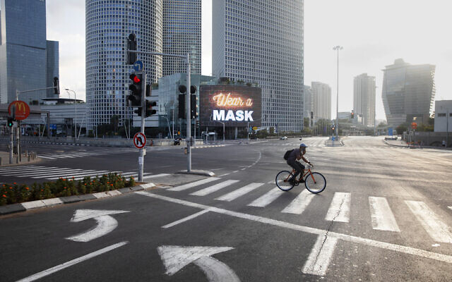 A man rides a bicycle next to a billboard calling people to wear masks, on empty road following new restrictions in the three-week nationwide lockdown, in Tel Aviv, Israel, Sept. 26, 2020. (AP Photo/Oded Balilty)