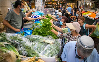 Israelis, wearing face masks for fear of the coronavirus, shop for groceries at the Mahane Yehuda market in Jerusalem on September 14, 2020. (Olivier Fitoussi/Flash90)