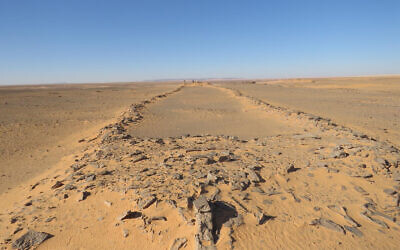 A massive, ancient stone structure in Saudi Arabia, with platforms at both ends and connecting walls in between. Two barely visible researchers standing at the far end provide a sense of scale. (courtesy/ Huw Groucutt/ The Holocene)
