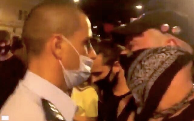 Jerusalem police officer Koby Yaakobi wears a mask with his nose exposed while standing among a crowd of protesters demonstrating against Prime Minister Benjamin Netanyahu outside his official residence in Jerusalem on Sunday, September 20, 2020. (Screen capture/Ynet News) Jerusalem police officer Koby Yaakobi wears a mask with his nose exposed while standing among a crowd of protesters demonstrating against Prime Minister Benjamin Netanyahu outside his official residence in Jerusalem on Sunday, September 20, 2020. (Screen capture/Ynet News)
