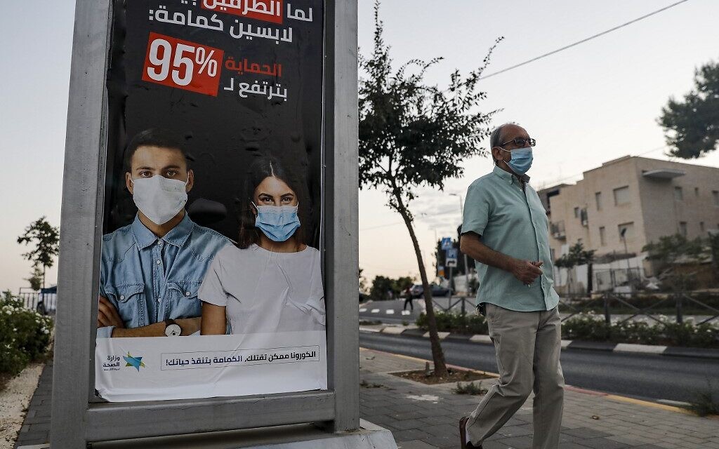A man walks past an advert sign posted by Israel's health ministry instructing people in Arabic to wear face masks as a prevention method of COVID-19 coronavirus disease in the Arab neighbourhood of Sheikh Jarrah in east Jerusalem on October 8, 2020. (Photo by Ahmad GHARABLI / AFP)