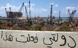 Arabic graffiti drawn on the side of a road reading "my government did this" is seen in front of the cranes at the port of Lebanon's capital Beirut, while in the background are the damaged grain silos opposite the blast site of a colossal explosion, August 9, 2020. (Patrick Baz/AFP)