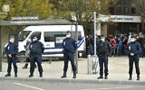 French police officers stand guard as adults and children gather in front of flowers displayed at the entrance of a middle school in Conflans-Sainte-Honorine, 30 kilometers northwest of Paris, on October 17, 2020, after a teacher was decapitated by an attacker who has been shot dead by policemen. (Bertrand Guay/AFP)