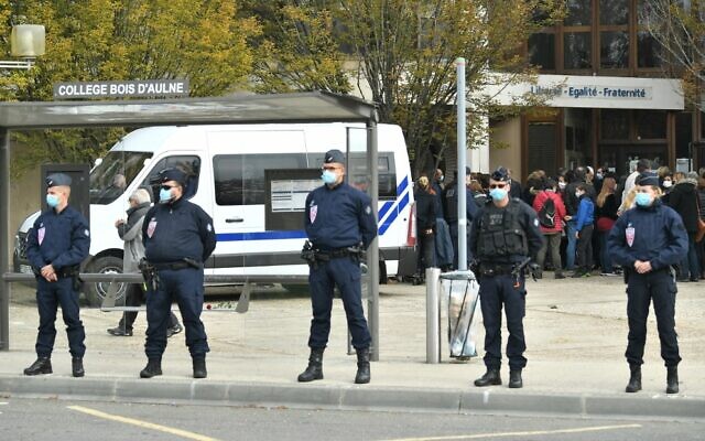 French police officers stand guard as adults and children gather in front of flowers displayed at the entrance of a middle school in Conflans-Sainte-Honorine, 30 kilometers northwest of Paris, on October 17, 2020, after a teacher was decapitated by an attacker who has been shot dead by policemen. (Bertrand Guay/AFP) French police officers stand guard as adults and children gather in front of flowers displayed at the entrance of a middle school in Conflans-Sainte-Honorine, 30 kilometers northwest of Paris, on October 17, 2020, after a teacher was decapitated by an attacker who has been shot dead by policemen. (Bertrand Guay/AFP)