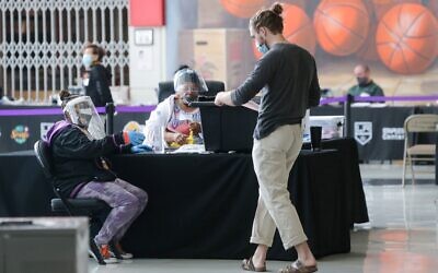 A voter (R) walks toward an election official who is wearing a face shield, mask and gloves at a Vote Center located at the Staples Center on the first weekend of early in-person voting on October 25, 2020 in Los Angeles, California. (Mario Tama/Getty Images/AFP)