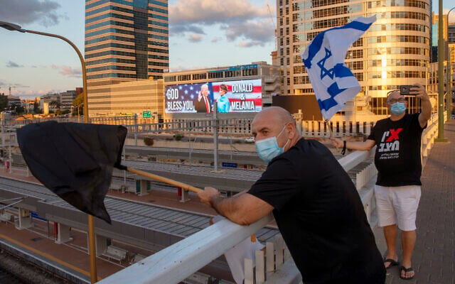 Backdropped by a billboard supporting US President Donald Trump and first lady Melania Trump, people wave flags on a bridge during a protest against Prime Minister Benjamin Netanyahu in Tel Aviv, October 3, 2020. (AP Photo/Oded Balilty) Backdropped by a billboard supporting US President Donald Trump and first lady Melania Trump, people wave flags on a bridge during a protest against Prime Minister Benjamin Netanyahu in Tel Aviv, October 3, 2020. (AP Photo/Oded Balilty)