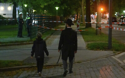 In this Oct. 4, 2020 photo a man and a boy walk towards the cordoned-off area in front of a synagogue in Hamburg, Germany that was the scene of an attack (Jonas Walzberg/dpa via AP)