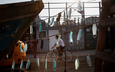A man wearing face mask rides his bicycle next to boats with face masks hanging on them during a nationwide lockdown to curb the spread of the coronavirus, at Jaffa port near Tel Aviv, October 7, 2020. (Oded Balilty/AP)