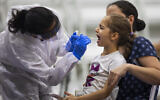 A young girl is tested for the coronavirus by a healthcare worker at a COVID-19 testing center set up at a basketball court, in Ramat Gan, October 20, 2020. (AP Photo/Oded Balilty)