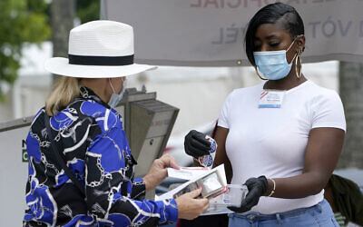 A woman drops off a vote-by-mail ballot with an election worker, right, at an official ballot drop box outside of an early voting site, October 20, 2020, in Miami Beach, Florida (AP Photo/Lynne Sladky) A woman drops off a vote-by-mail ballot with an election worker, right, at an official ballot drop box outside of an early voting site, October 20, 2020, in Miami Beach, Florida (AP Photo/Lynne Sladky)