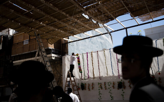 Men hang decorations in a newly built sukkah in the ultra-Orthodox neighborhood of Mea Shearim in Jerusalem on October 2, 2020 (Nati Shohat/Flash90) Men hang decorations in a newly built sukkah in the ultra-Orthodox neighborhood of Mea Shearim in Jerusalem on October 2, 2020 (Nati Shohat/Flash90)