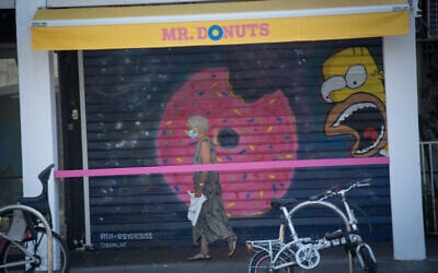 A woman walks past a closed store in Tel Aviv during a nationwide coronavirus lockdown, October 13, 2020. (Miriam Alster/Flash90)