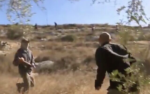 A settler with a cudgel (L) attacks Channel 12 news reporter Ohad Hemo during clashes with Palestinian olive harvesters in the West Bank village of Burka, October 13, 2020. (Screen capture: Twitter)
