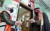A voter is assisted by a volunteer to put on a plastic glove before entering a polling station in Jordan's capital Amman on November 10, 2020. (Khalil MAZRAAWI / AFP)