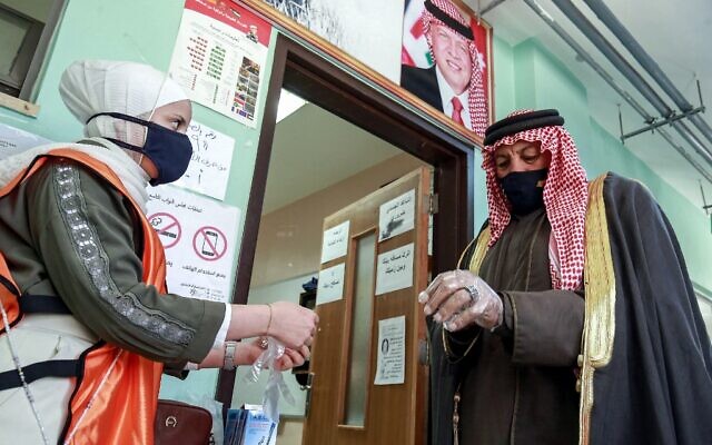 A voter is assisted by a volunteer to put on a plastic glove before entering a polling station in Jordan's capital Amman on November 10, 2020. (Khalil MAZRAAWI / AFP) A voter is assisted by a volunteer to put on a plastic glove before entering a polling station in Jordan's capital Amman on November 10, 2020. (Khalil MAZRAAWI / AFP)