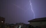 This picture taken from Gaza City shows lightning flashing over buildings as the flare of a rocket launch is seen nearby during a thunderstorm in Gaza city on November 15, 2020. (MOHAMMED ABED / AFP)
