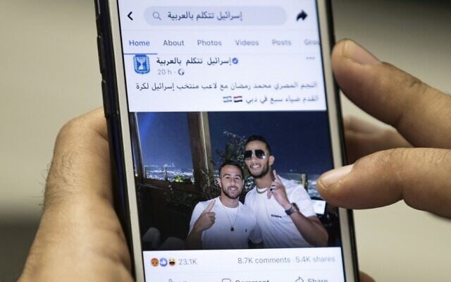 A man in Cairo holds a phone showing a picture of Egyptian singer Mohamed Ramadan posted by the official Facebook page of the State of Israel in Arabic showing Ramadan, right, hugging Israeli soccer player Diaa Sabia in Dubai, November 22, 2020. (Khaled Desouki/AFP) A man in Cairo holds a phone showing a picture of Egyptian singer Mohamed Ramadan posted by the official Facebook page of the State of Israel in Arabic showing Ramadan, right, hugging Israeli soccer player Diaa Sabia in Dubai, November 22, 2020. (Khaled Desouki/AFP)