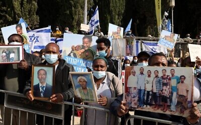 Members of the Jewish Ethiopian community hold up photographs of their relatives outside the Prime Minister's Office in Jerusalem on November 25, 2020, during a demonstration demanding to bring thousands of their remaining brethren from Ethiopia to Israel. (Menahem Kahana/AFP)