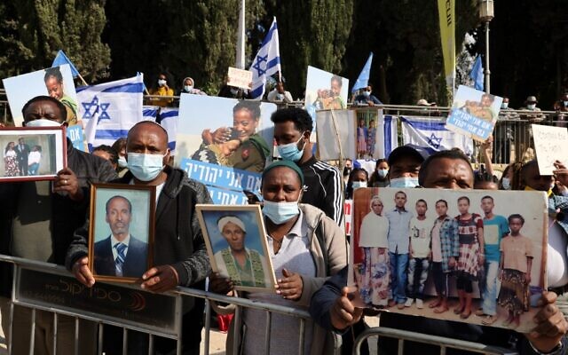 Members of the Jewish Ethiopian community hold up photographs of their relatives outside the Prime Minister's Office in Jerusalem on November 25, 2020, during a demonstration demanding to bring thousands of their remaining brethren from Ethiopia to Israel. (Menahem Kahana/AFP)