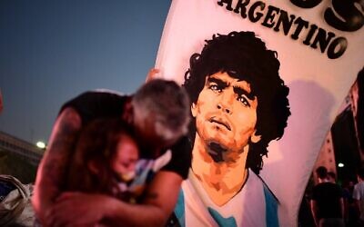 A father and her daughter, fans of Argentinian football legend Diego Maradona, mourn as they gather by the Obelisk to pay homage on the day of his death in Buenos Aires, on November 25, 2020. (Photo by RONALDO SCHEMIDT / AFP)