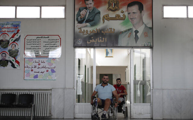In this Sunday, Oct. 7, 2018 photo, Syrian soldiers who lost their legs while fighting in Syria's war, wheel past a poster showing Syrian President Bashar Assad, after a physical therapy session at the Ahmad Hamish Martyr hospital, in Damascus, Syria. (AP/Hassan Ammar) In this Sunday, Oct. 7, 2018 photo, Syrian soldiers who lost their legs while fighting in Syria's war, wheel past a poster showing Syrian President Bashar Assad, after a physical therapy session at the Ahmad Hamish Martyr hospital, in Damascus, Syria. (AP/Hassan Ammar)