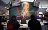 ILLUSTRATIVE -- An image of 'Crypto,' the main character in the video game 'Destroy All Humans!,' appears above people playing video games at the THQ Nordic exhibit, Feb. 27, 2020, at the Pax East conference in Boston. (AP Photo/Steven Senne)