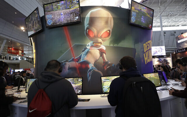 ILLUSTRATIVE -- An image of 'Crypto,' the main character in the video game 'Destroy All Humans!,' appears above people playing video games at the THQ Nordic exhibit, Feb. 27, 2020, at the Pax East conference in Boston. (AP Photo/Steven Senne) ILLUSTRATIVE -- An image of 'Crypto,' the main character in the video game 'Destroy All Humans!,' appears above people playing video games at the THQ Nordic exhibit, Feb. 27, 2020, at the Pax East conference in Boston. (AP Photo/Steven Senne)