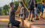 A man helping a child with her mask as children make their way to school in Moshav Yashresh, on November 1, 2020. (Yossi Aloni/Flash90)