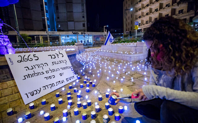 People stand next to LED candles placed by activists from the "Darkenu" movement in memory of Israel's coronavirus victims, near the prime minister's official residence in Jerusalem on November 8, 2020. The poster says the number of dead has reached the level of those killed in the 1973 Yom Kippur War and calls for a commission of inquiry. (Olivier Fitoussi/Flash90) People stand next to LED candles placed by activists from the "Darkenu" movement in memory of Israel's coronavirus victims, near the prime minister's official residence in Jerusalem on November 8, 2020. The poster says the number of dead has reached the level of those killed in the 1973 Yom Kippur War and calls for a commission of inquiry. (Olivier Fitoussi/Flash90)