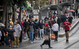 People wearing face masks take cover from the rain on Jaffa Street in downtown Jerusalem, on November 11, 2020. (Yonatan Sindel/Flash90)