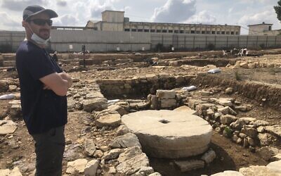 Excavation director Yevgeny Aharonovich stands next to an unused Second Temple-era olive press at the ancient settlement of Kafr Murr, today a neighborhood of Beit El, November 3, 2020. (Amanda Borschel-Dan/ToI)