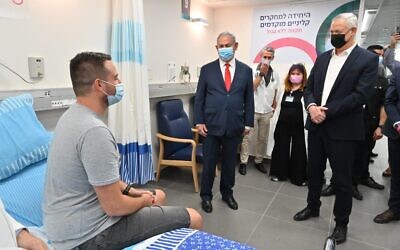 Prime Minister Benjamin Netanyahu (C) and Defense Minister Benny Gantz (R) speak with Segev Harel, the first volunteer for trials for an experimental Israeli coronavirus vaccine, at Sheba Medical Center, November 1, 2020. (Ariel Hermoni/Defense Ministry)