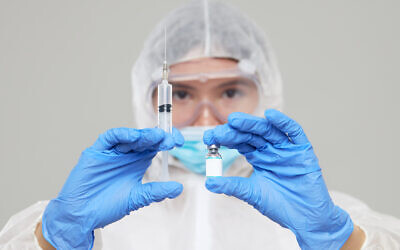 A medic in a protective suit and mask holds an injection syringe and vaccine. (oshcherban via iStock by Getty Images)