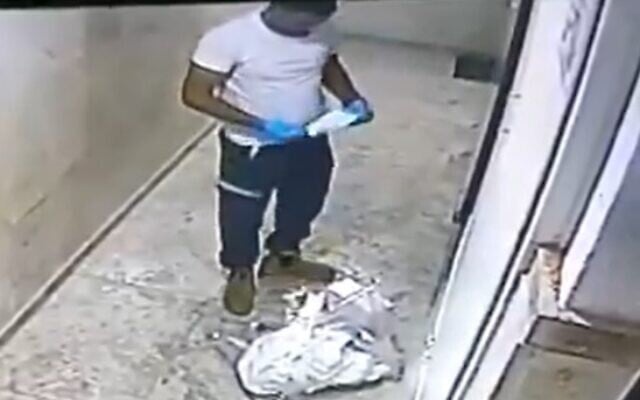 A worker for the Magen David Adom emergency service replaces his mask after spitting on pictures of Jesus and Mary in a residential building in Jaffa, November 15, 2020 (Screen grab/Kan) A worker for the Magen David Adom emergency service replaces his mask after spitting on pictures of Jesus and Mary in a residential building in Jaffa, November 15, 2020 (Screen grab/Kan)