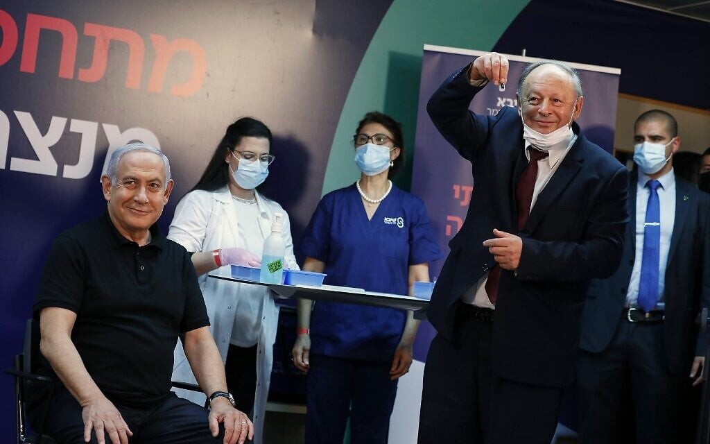 Prime Minister Benjamin Netanyahu smiles before receiving a coronavirus vaccine at Sheba Medical Center in Ramat Gan from his personal physician, Dr. Tzvi Berkovitz. Netanyahu, 71, followed by Health Minister Yuli Edelstein, became the first Israelis to get the vaccine. (AMIR COHEN / POOL / AFP) Prime Minister Benjamin Netanyahu smiles before receiving a coronavirus vaccine at Sheba Medical Center in Ramat Gan from his personal physician, Dr. Tzvi Berkovitz. Netanyahu, 71, followed by Health Minister Yuli Edelstein, became the first Israelis to get the vaccine. (AMIR COHEN / POOL / AFP)