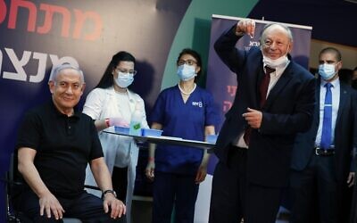 Prime Minister Benjamin Netanyahu (L) smiles before receiving a coronavirus vaccine, from his personal physician Dr. Tzvi Berkovitz, at Sheba Medical Center in Ramat Gan on December 19, 2020. At center in background (in blue scrubs) is nurse Shoshi Gomel (Amir Cohen/Pool/AFP)