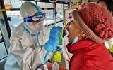 A Chinese health worker (L) in a protective suit takes a swab from a Dalian resident to test for coronavirus, as the city carries out a mass testing program after new confirmed cases were found, in northeastern China's Liaoning province, on December 23, 2020. (Stringer/AFP)