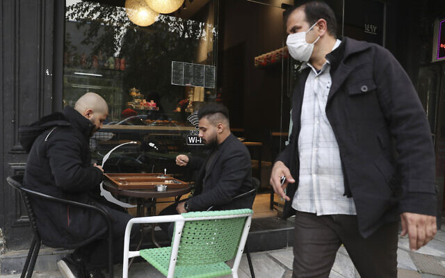 Two men play backgammon outside a cafe as a man wearing a protective face mask to help prevent the spread of the coronavirus walks past, in downtown Tehran, Iran, December 5, 2020. (AP Photo/Vahid Salemi) Two men play backgammon outside a cafe as a man wearing a protective face mask to help prevent the spread of the coronavirus walks past, in downtown Tehran, Iran, December 5, 2020. (AP Photo/Vahid Salemi)