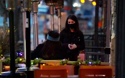 A waitperson wears a face mask while tending to a patron sitting in the outdoor patio of a sushi restaurant, late December 28, 2020, in downtown Denver, Colorado. (AP Photo/David Zalubowski)