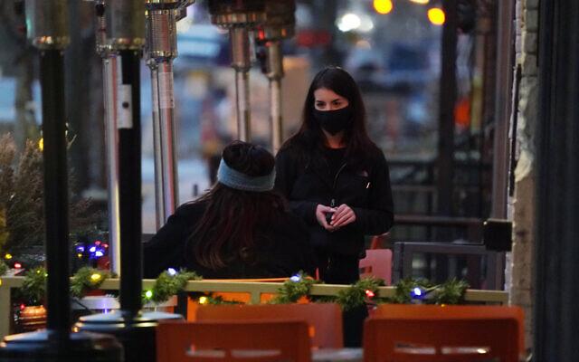A waitperson wears a face mask while tending to a patron sitting in the outdoor patio of a sushi restaurant, late December 28, 2020, in downtown Denver, Colorado. (AP Photo/David Zalubowski) A waitperson wears a face mask while tending to a patron sitting in the outdoor patio of a sushi restaurant, late December 28, 2020, in downtown Denver, Colorado. (AP Photo/David Zalubowski)