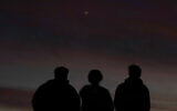 People are silhouetted against the sky at dusk as they watch the alignment of Saturn and Jupiter, December 21, 2020, in Edgerton, Kansas. (AP Photo/Charlie Riedel)