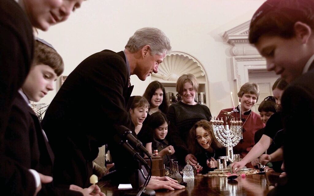 Following the lighting of the menorah on the first night of Hanukkah on December 23, 1997, President Clinton leans over his desk in the Oval Office as children from the Jewish Primary Day School in Washington show him how to twirl the dreidel, a traditional toy similar to a spinning top. (AP/J. Scott Applewhite)