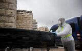 Chevra Kadisha workers wearing protective clothing carry the body of a patient who died from complications of COVID-19 at the Shamgar Funeral Home in Jerusalem on April 1, 2020 (Yonatan Sindel/Flash90)